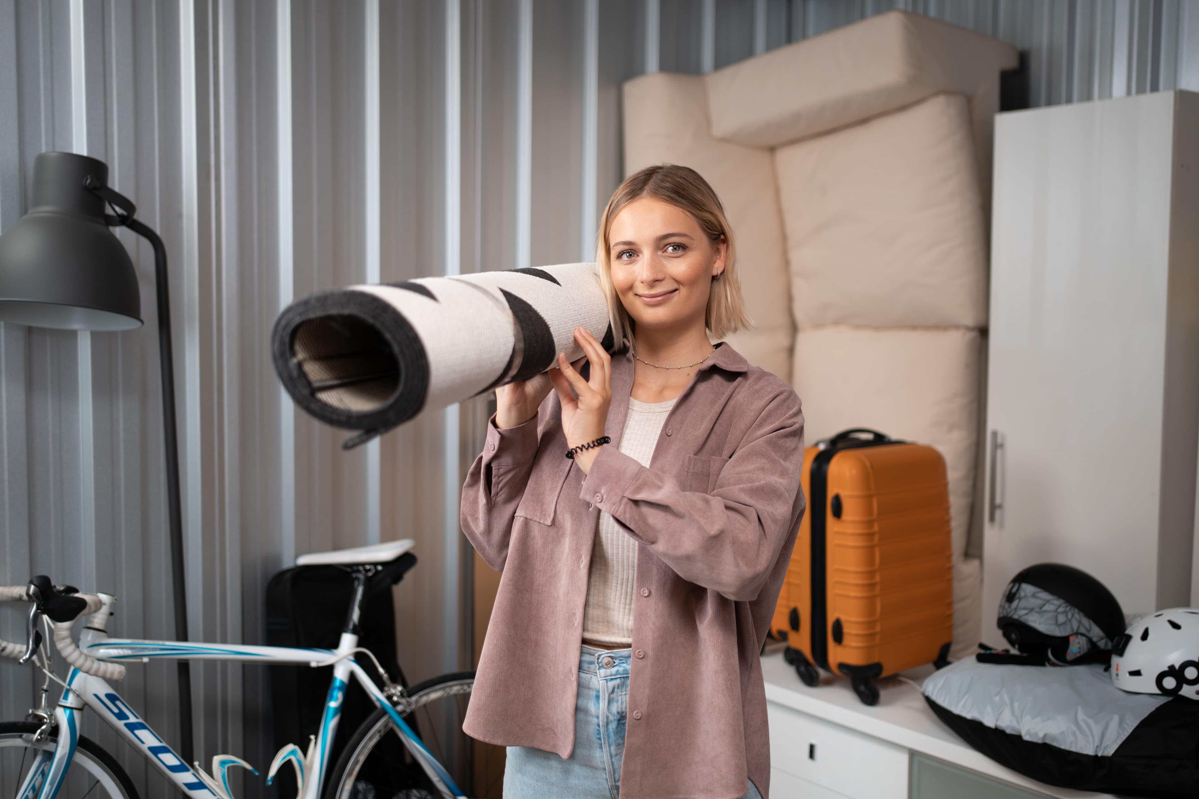 A young woman is holding a carpet on her shoulder and is standing in her Zebrabox storage unit.