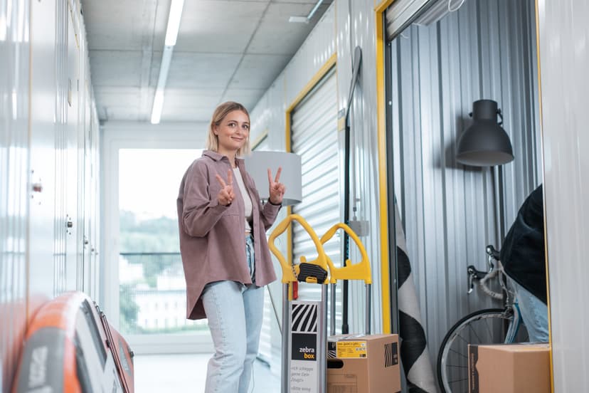 Une jeune femme se tient devant son espace de stockage de Zebrabox et sourit à la caméra.