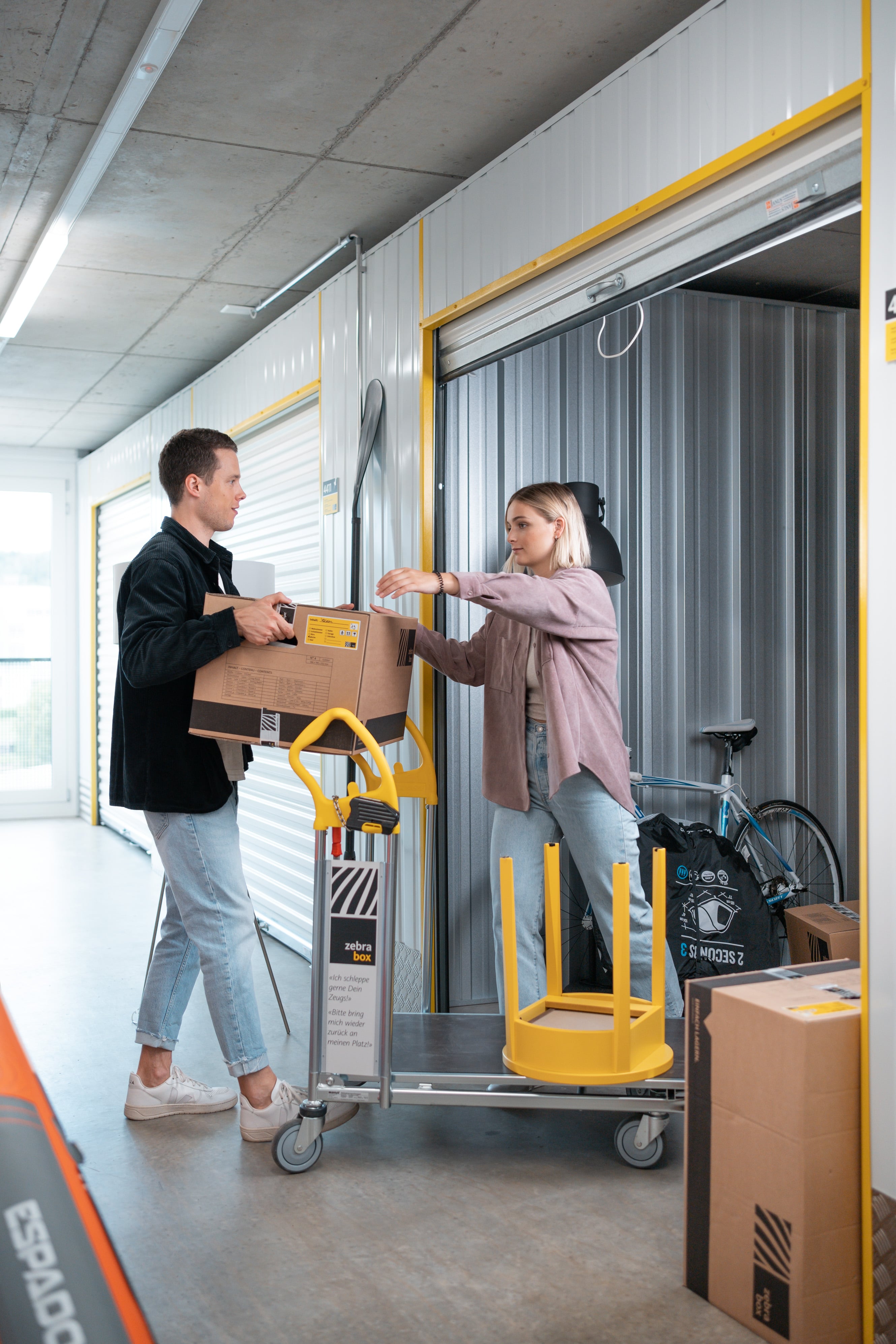 Un jeune couple se tient dans le couloir de Zebrabox et range des objets dans l'espace de stockage.