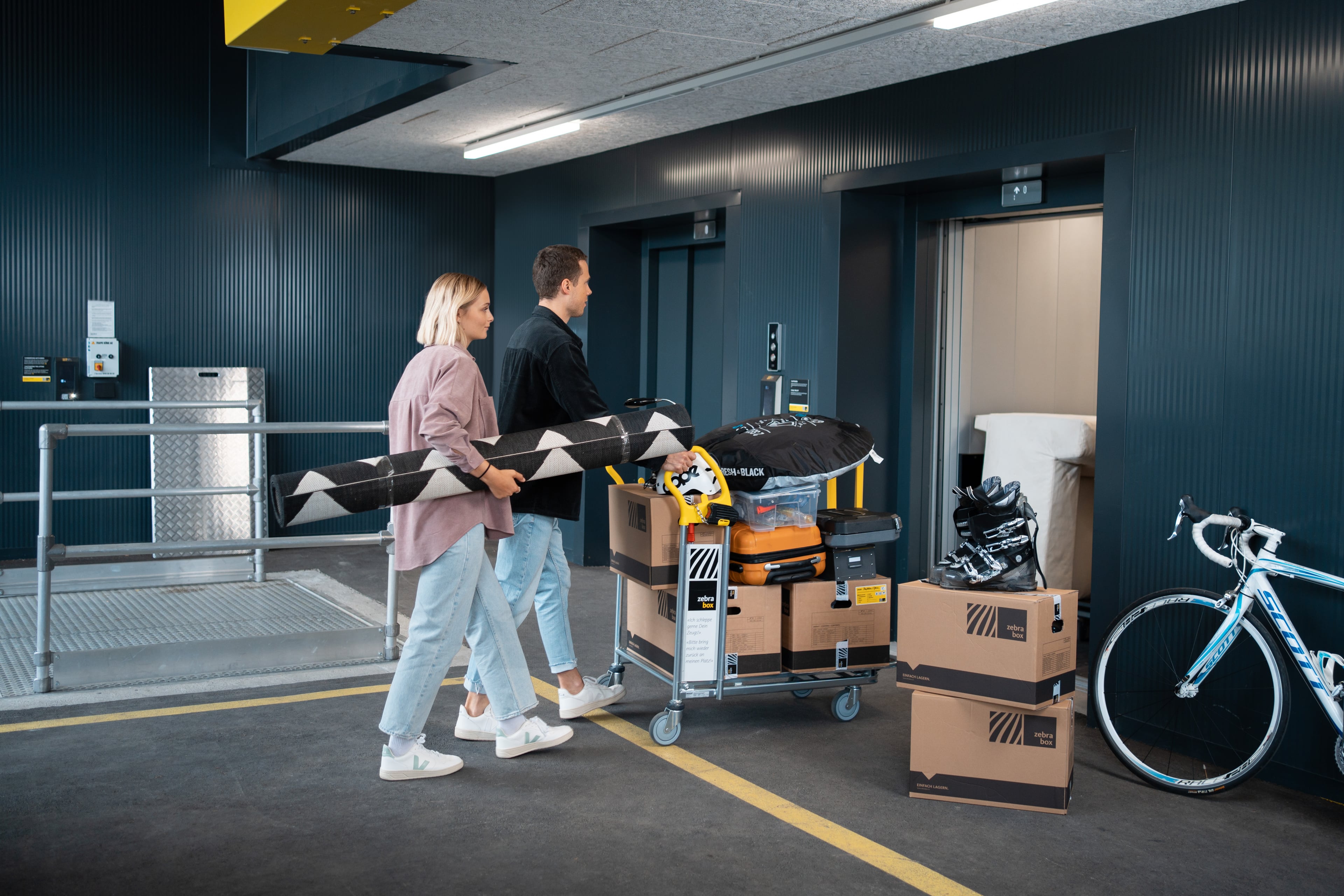 Un jeune couple transporte du mobilier et des caisses de déménagement dans l'ascenseur de charge de Zebrabox.