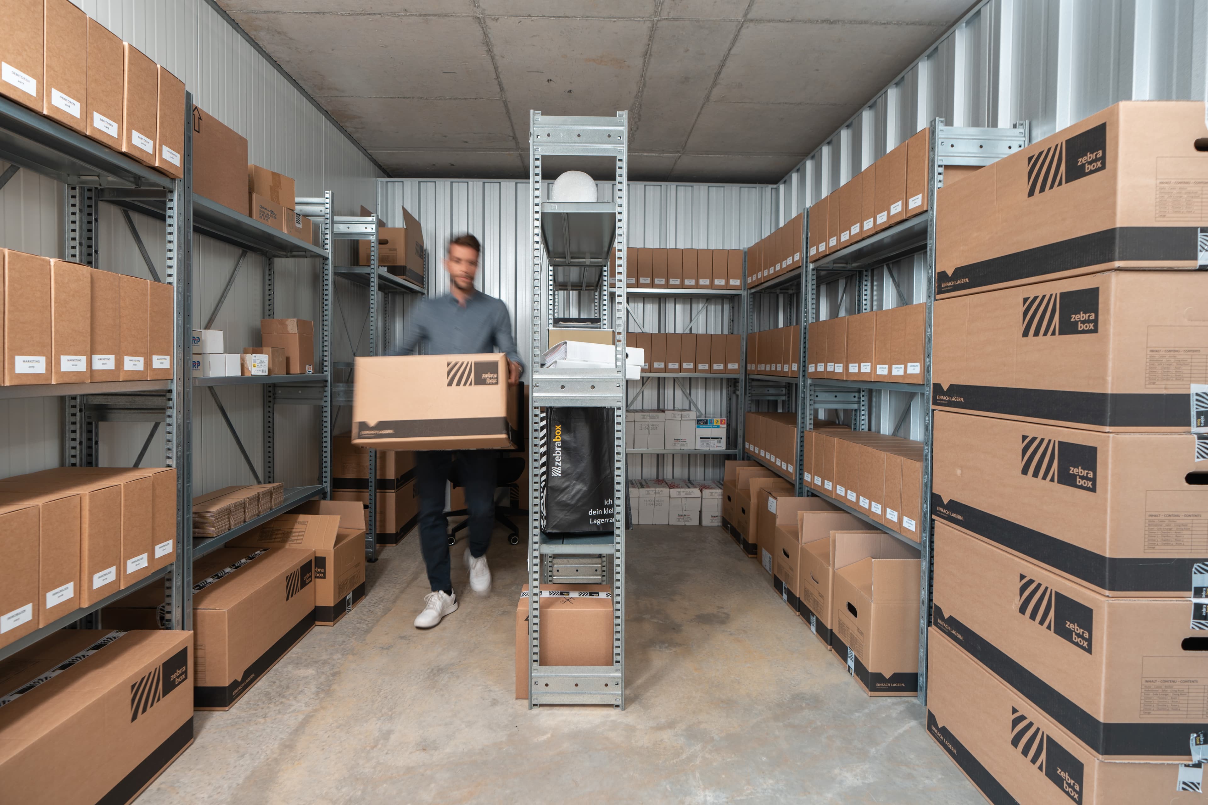 A man is walking through the Zebrabox storage unit with a moving box.