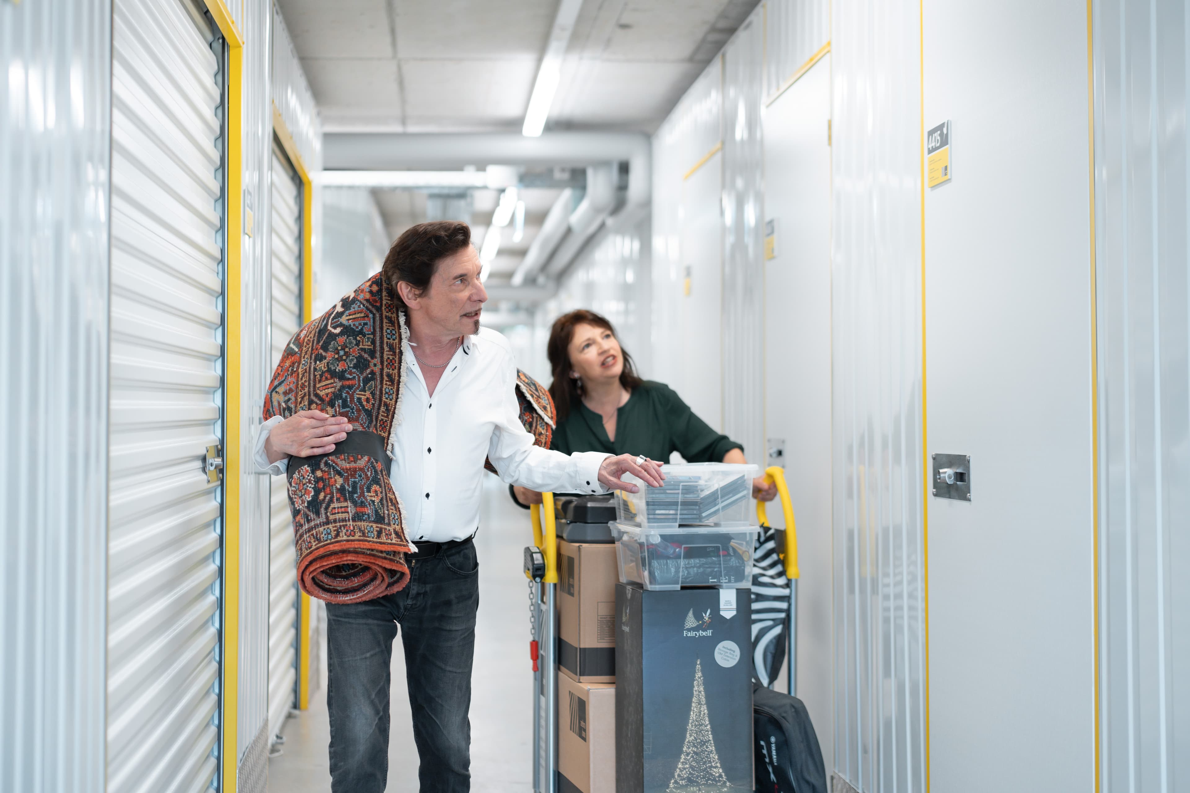 An elderly couple is walking through the Zebrabox warehouse with a filled trolley to store their household goods.