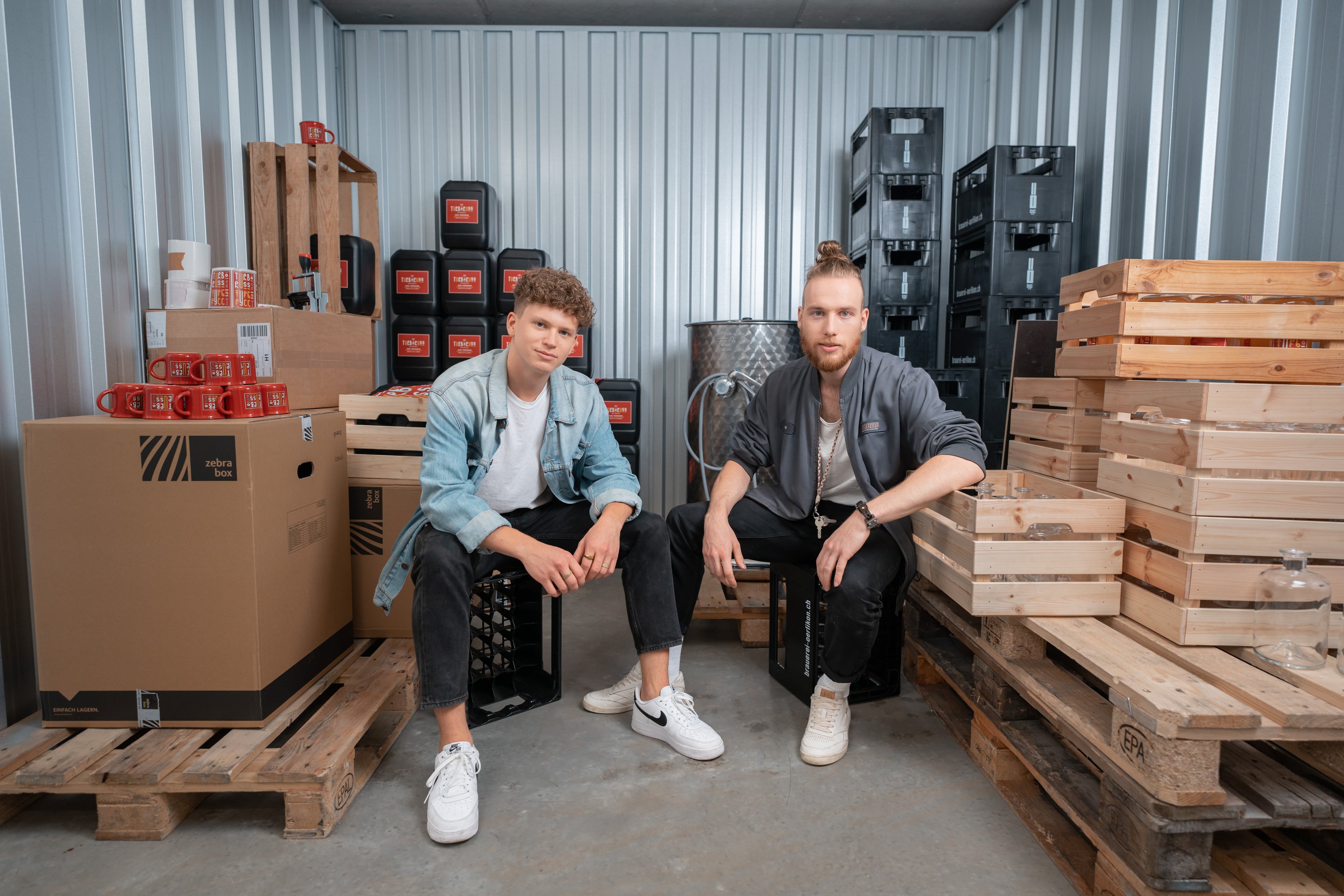 Two young start-up founders of a brewery are sitting in the Zebrabox storage unit and looking happily into the camera.