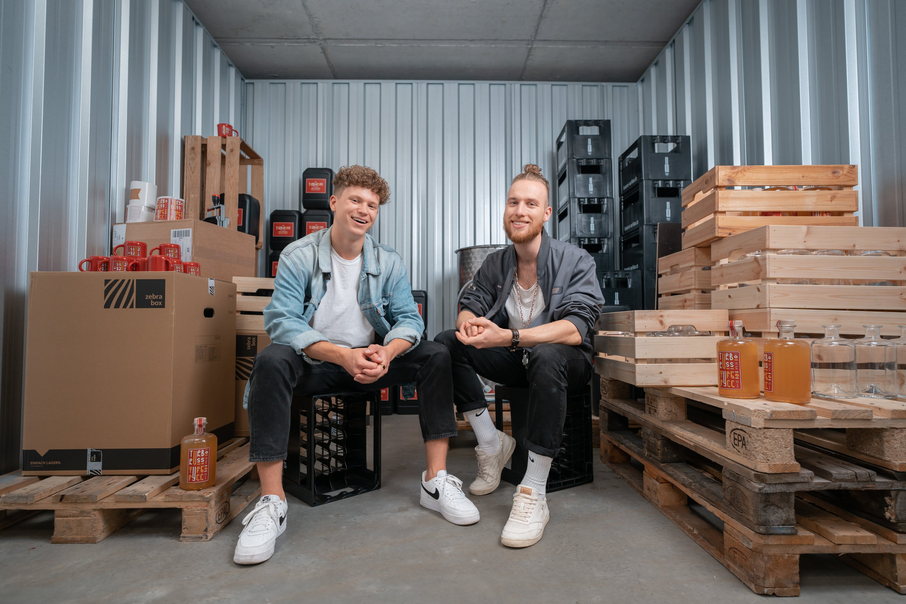 Deux jeunes fondateurs d’une startup brassicole sont assis dans l'espace de stockage de Zebrabox et regardent joyeusement la caméra.