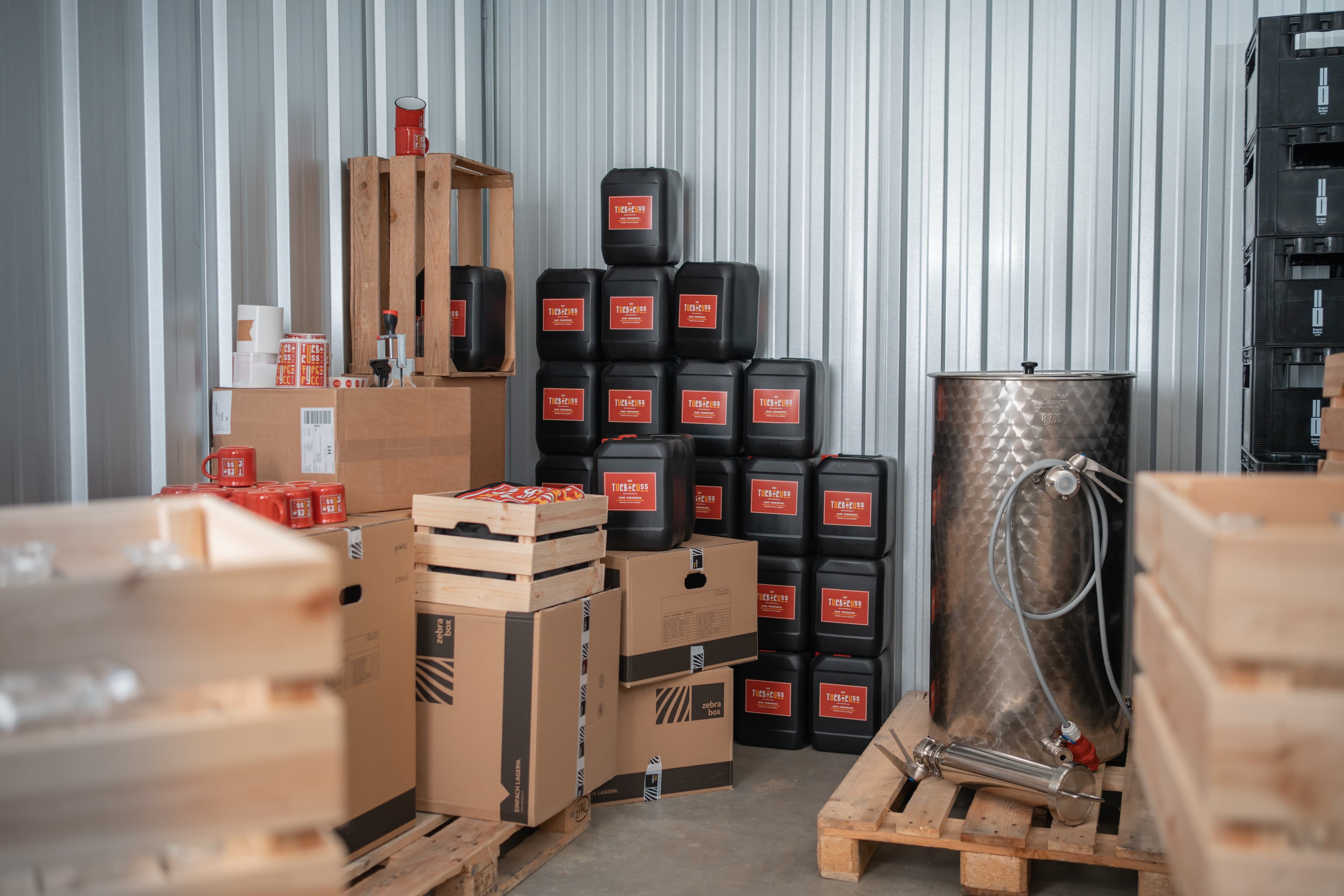 In a Zebrabox storage unit, a company's warehouse is visible with beverage cans, wooden crates, moving boxes and wooden pallets.