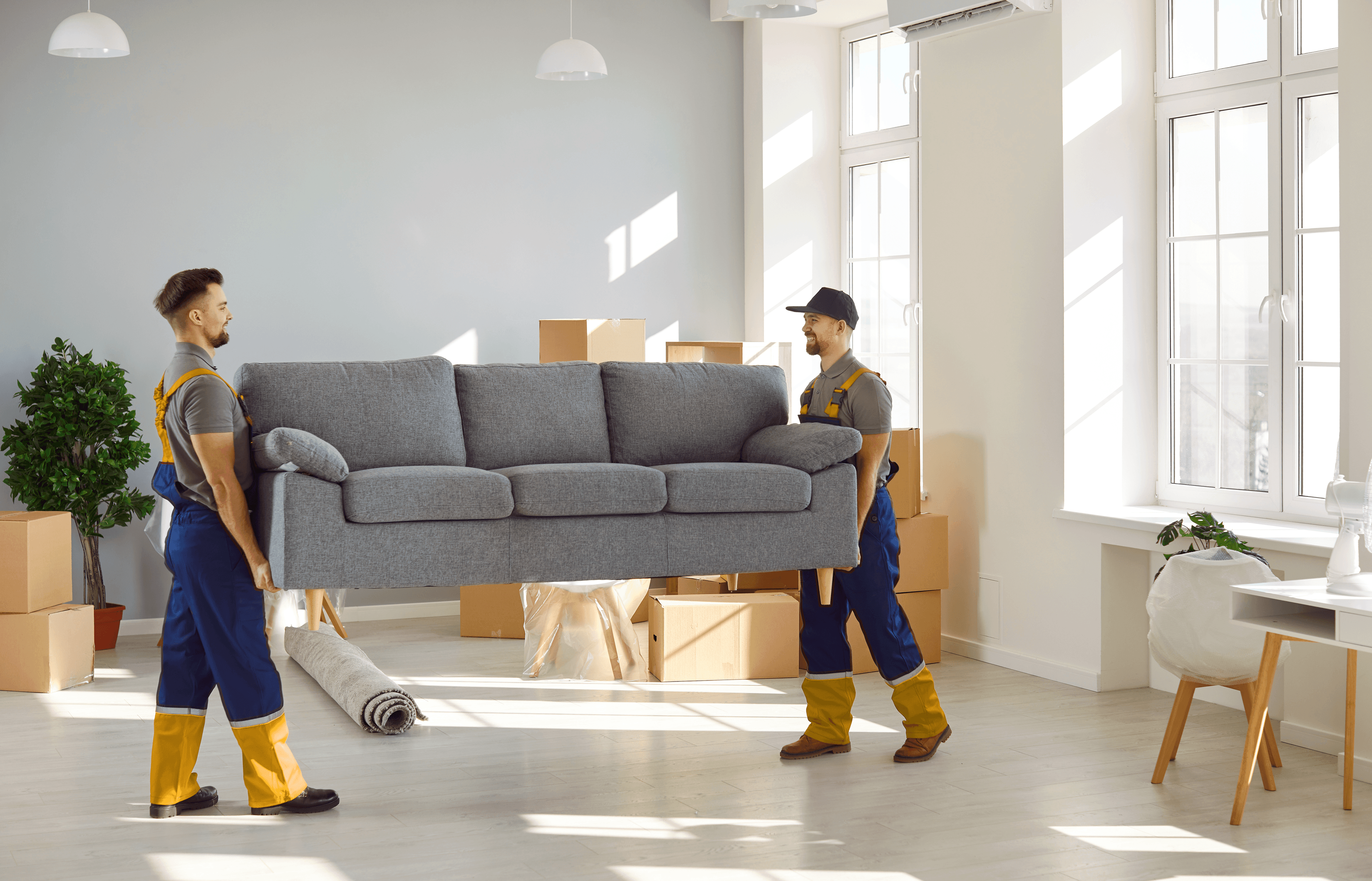 Two men from a moving company are carrying a sofa in a living room.